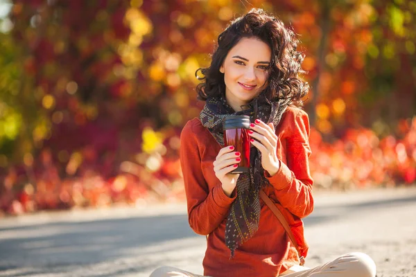 Young beautiful woman with cup of tea or coffee at autumn background. Portrait of attractive young girl outdoors
