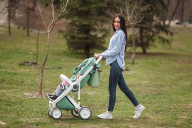 Genç neşeli anne çocuğunu carriege ile yürüme