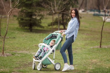 Genç neşeli anne çocuğunu carriege ile yürüme