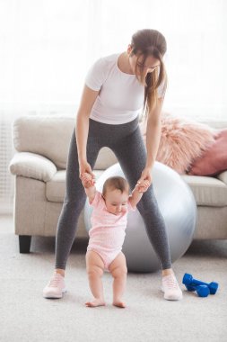 Young pretty mother working out with her little child at home clipart