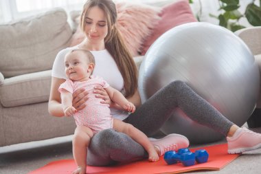 Young pretty mother working out with her little child at home clipart