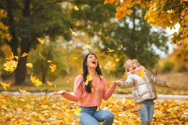Neşeli kızlar sarı yaprakları ile oynuyor. Mutlu anne ve eğleniyor sonbahar zamanla küçük çocuk
