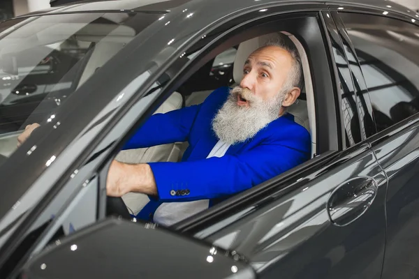 Old stylish man in the luxury car. Male with beard and mustash driving automobile. car sales salon.