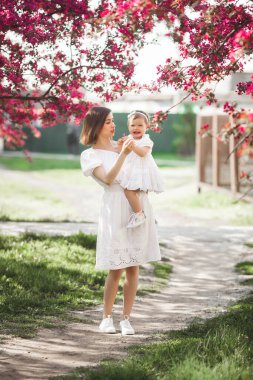Küçük tatlı kızıyla bahar bahçesinde yürüyen genç ve güzel bir anne. Anne ve çocuk bahar çiçeklerinde eğleniyorlar. Aile dışarıda bir arada..