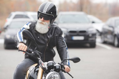 Motosiklet süren olgun bir adam. Motosikletli yaşlı bir erkek. Sakallı adam dışarıda araba sürüyor..