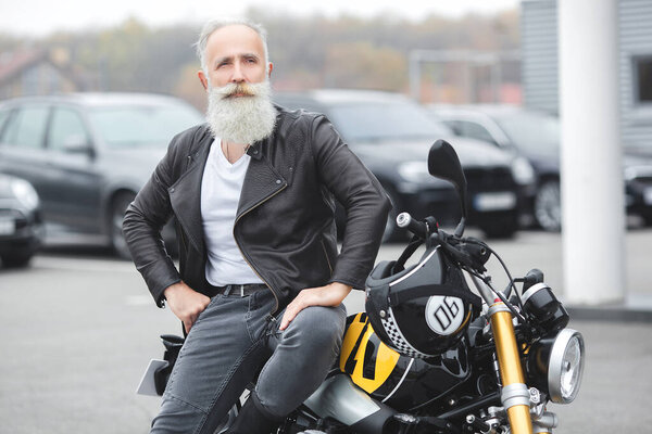 Mature man riding a motorcycle. Old male on motorbike. Bearded man outdoors driving.