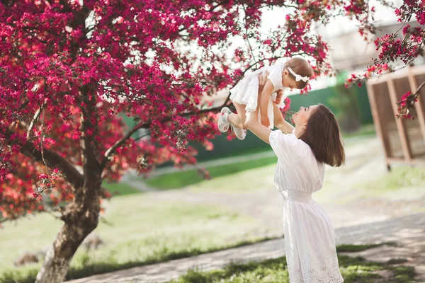 可愛い娘と春の庭を歩いている若い可愛い母親 春の花でお母さんと子供が楽しんでいます 一緒に屋外の家族 — ストック写真