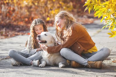 Golden Retriever 'lı güzel kızlar. Dışarıda eğlenen iki kız kardeş. Sonbahar arka planında hayvan sahipleri..