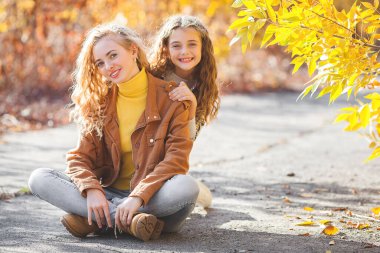 Sonbahar arka planında birlikte yürüyen iki güzel kız kardeş. Neşeli kızlar. Sonbahar kavramı.