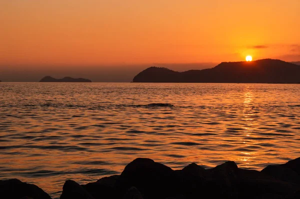 Sol si se esconde detrás de la montaña a lo largo del mar Fotos de stock