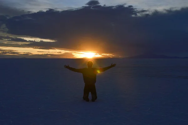 Man kneeling at Salar de Uyuni in Bolivia at sunset time