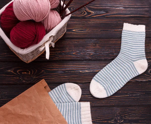 Wicker basket filled with wool and yarn with striped white socks on a dark wooden background — Stock Photo, Image