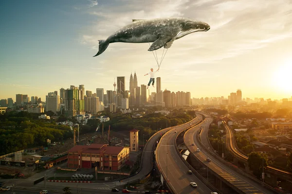 Homme et grande baleine survolant le paysage urbain — Photo