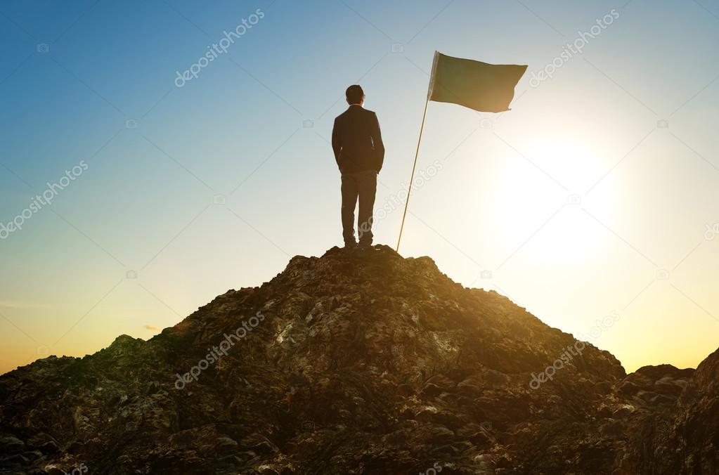 Silhouette of businessman with flag on mountain top
