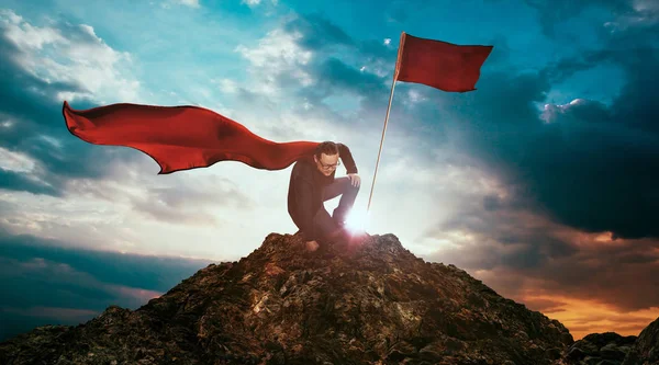 Businessman in cape hero on top of a mountain — Stock Photo, Image