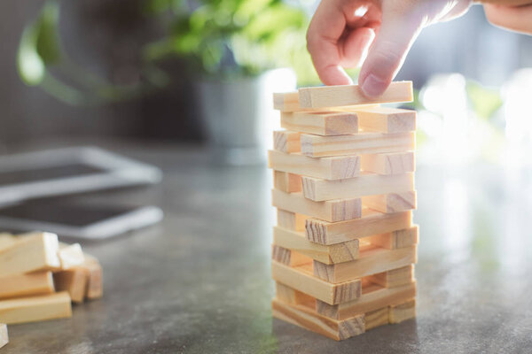 Hand of kid playing a blocks wood tower game of architectural project with sun flare and blur background .Selected focusing .