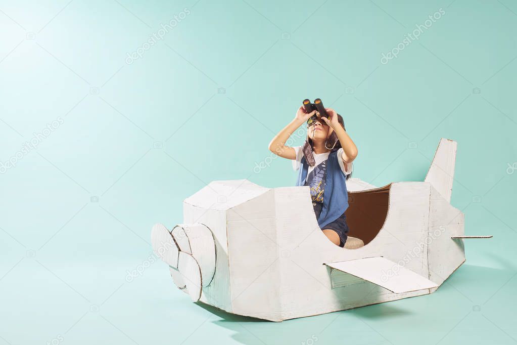 Little cute girl playing with a cardboard airplane. White retro style cardboard airplane on mint green background . Childhood dream imagination concept .