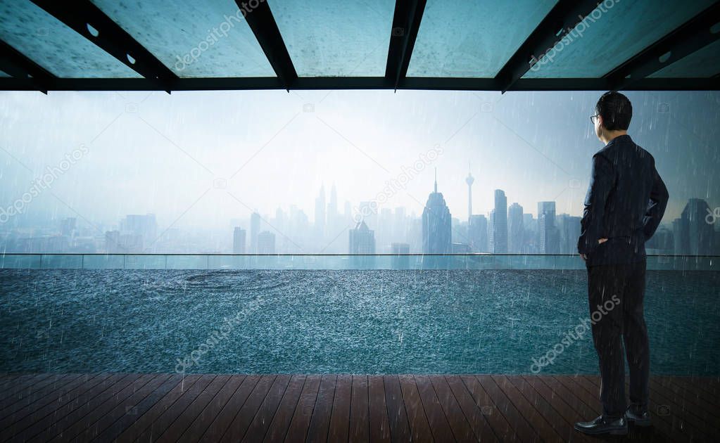 Businessman looking and thinking front of a Swimming pool on roof top with beautiful city skyline view,rainin