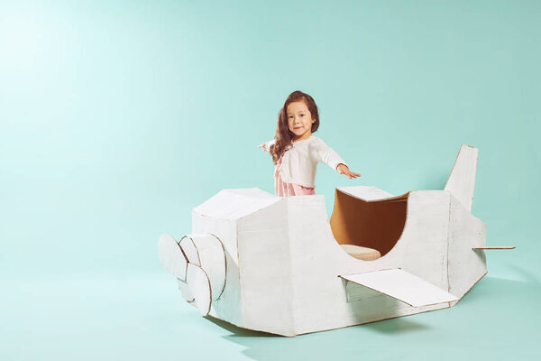 Маленькая милая девочка играет с картонным самолетом. White retro style cardboard airplane on mint green background. Детская фантазия
 .