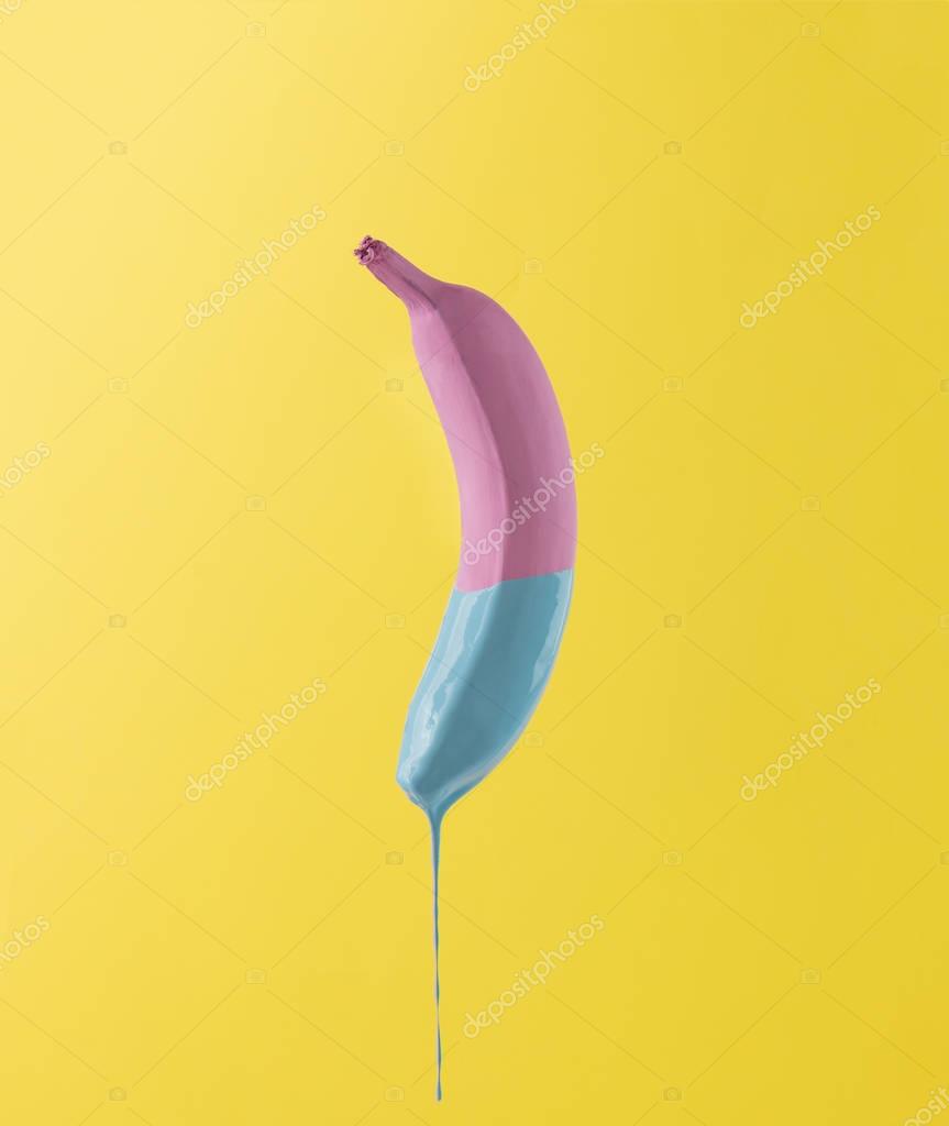 Pink banana with dripping blue paint on yellow background. Minimal food concept