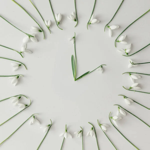 creative layout made with clock in form of snowdrop flowers on bright background, spring minimal concept