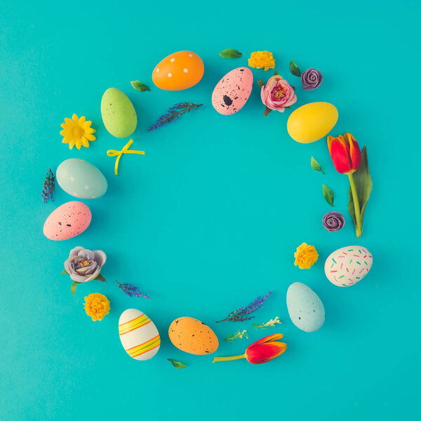 creative Easter layout in form of circle wreath made of colorful eggs and flowers on blue background 