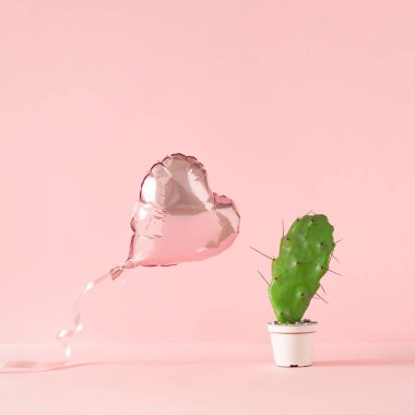 Heart shaped foil balloon with cactus plant on pink background. Creative valentine day concept.