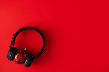 Wireless headphones and Christmas bauble decoration on red background. Creative Holiday party concept