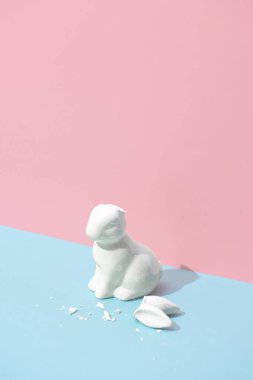 Kulakları kırık bir Paskalya tavşanı. Minimal pastel pembe ve mavi Paskalya bayramı konsepti. Çağdaş biçim.