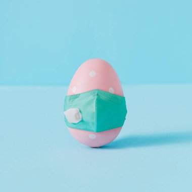Pembe Paskalya yumurtası ve virüs maskeli yaratıcı kompozisyon. Minimal Corona virüs salgını tatil konsepti. Pastel eğlenceli arkaplan.