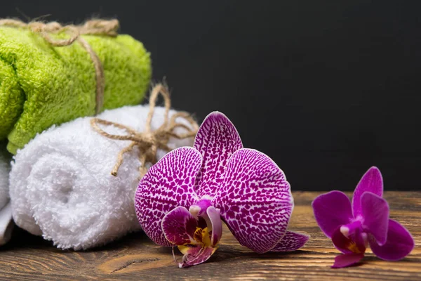 Orquídea junto a diferentes toallas en una mesa oscura, lugar superior para una inscripción — Foto de Stock