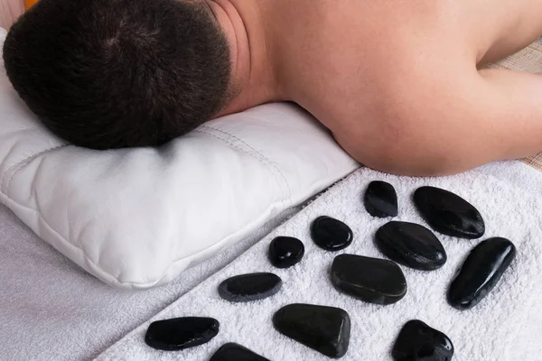 Black hot stones lie on a massage table before men — Stock Photo, Image