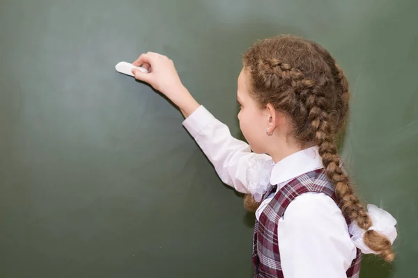 Meisje in school uniform schrijft met krijt op blackboard — Stockfoto