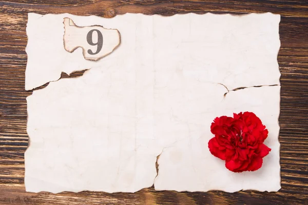 Trozo de papel quemado sobre la mesa, con un clavel rojo y el número 9 — Foto de Stock