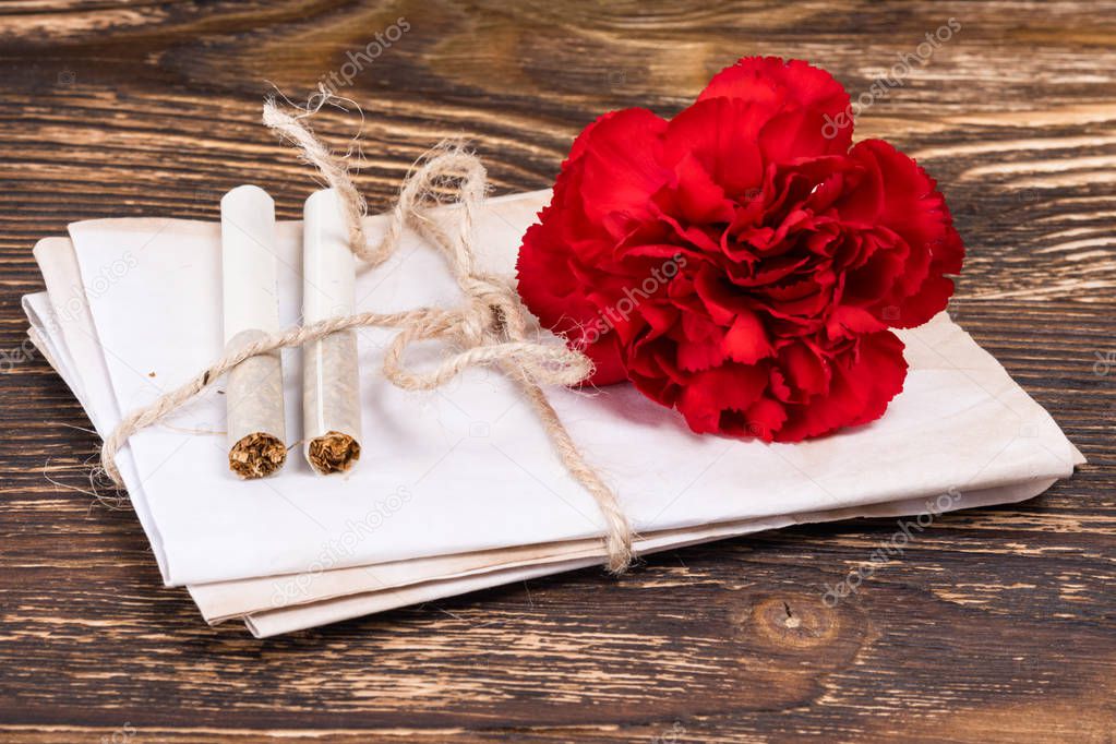 On a wooden table, bandaged documents and two cigarettes next to a carnation