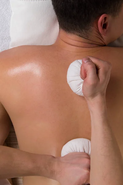 Strong hands doing massage with herbal bags — Stock Photo, Image