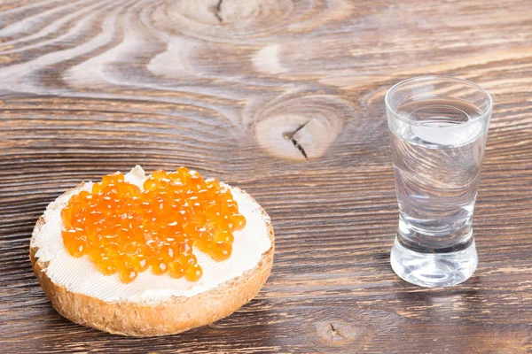 Sanduíche com manteiga e linha de caviar vermelho com um copo de vodka — Fotografia de Stock