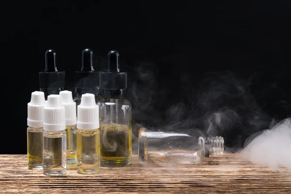 Öl in Flaschen für Parfüm und elektronische Zigaretten, auf dunklem Hintergrund — Stockfoto
