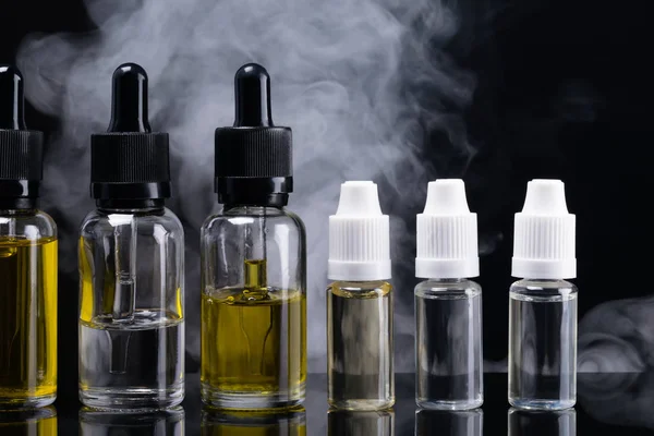 Zes containers van aromatische vloeistoffen op een zwarte achtergrond omgeven door rook — Stockfoto