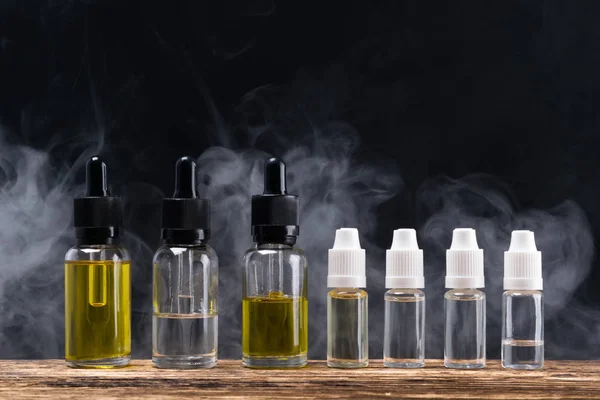 Liquido dagli aromi saporiti in bottiglia per una sigaretta elettronica, sullo sfondo del vapore — Foto Stock