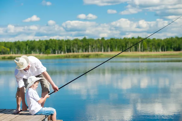 The father teaches his son, to fish on the river from the pier — Stock Photo, Image