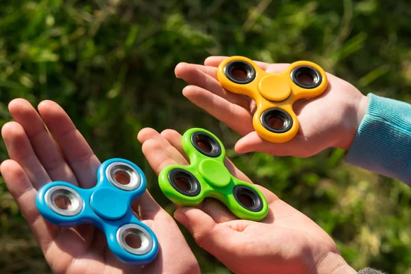 Spinner of different colors lie in the hands of children against the background of grass — Stock Photo, Image