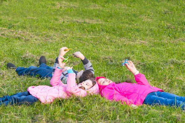 Två flickor och en pojke ligga i gräset och spela spinner — Stockfoto