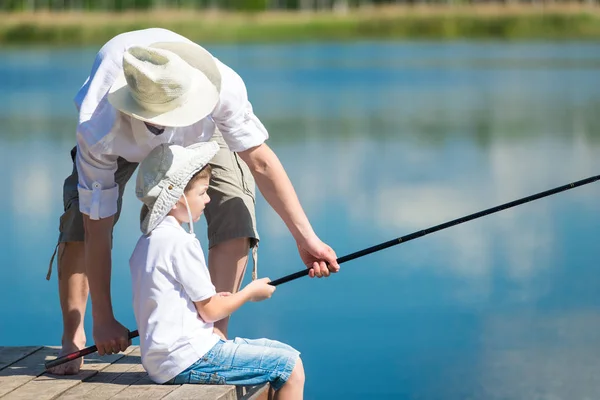 Papá ayuda a su hijo a pescar con una caña de pescar en el río —  Fotos de Stock