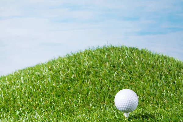 Bola blanca se encuentra en una clavija pegada en un césped para un juego de golf, contra un fondo de cielo azul —  Fotos de Stock