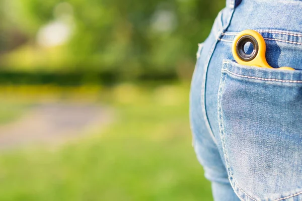 Spinner lies in the jeans pocket, in the background of the park — Stock Photo, Image