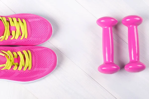 Conjunto rosa de mancuernas y zapatillas de deporte sobre un fondo gris madera — Foto de Stock