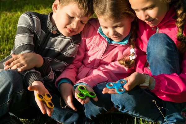 Tre barn sitter på gräset spelar en ny leksak spinner — Stockfoto