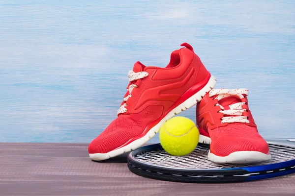 Kırmızı spor ayakkabıları üzerinde mavi bir arka plan üzerinde bir tenis raketi