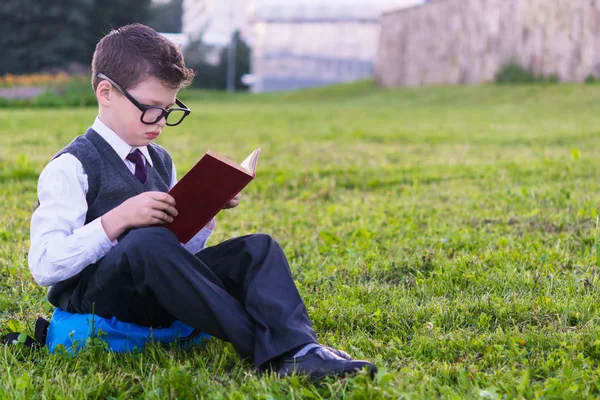 Élève dans des lunettes lit un livre assis sur l'herbe — Photo